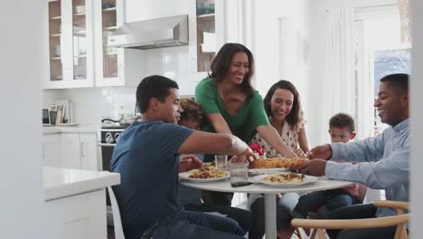 Middle-aged-grandmother-serving-mixed-race-multi-generation-family-eating-together-in-the-kitchen