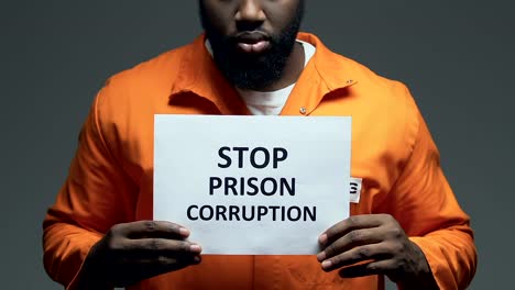 Stop-prison-corruption-phrase-on-cardboard-in-hands-of-black-prisoner,-disorder