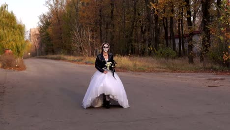 Chica-en-vestido-de-novia-con-una-máscara-de-cráneo-en-su-cara-está-corriendo-en-un-camino-vacío