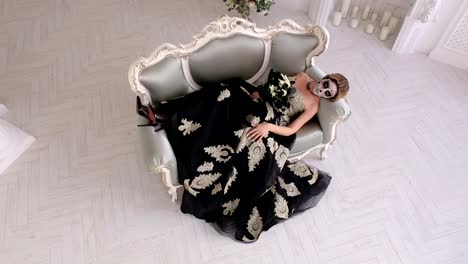 Creepy-woman-in-dress-and-with-makeup-in-the-form-of-skull-lies-on-a-retro-sofa
