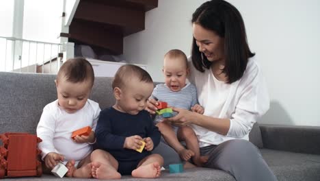 Asiatische-Triplets-spielen-auf-Couch-mit-Mutter