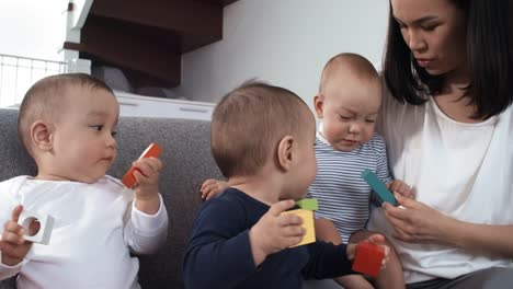 Gemischte-Rennen-Baby-Triplets-sitzen-auf-Couch-mit-Mutter