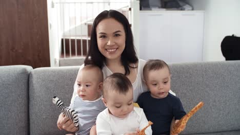 Mixed-Race-Mutter-posiert-mit-ihren-Triplets-auf-Couch