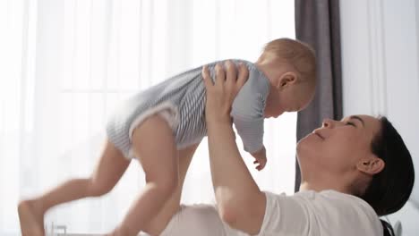 Glückliche-asiatische-Mutter-kuscheln-ihr-Baby