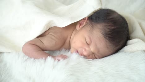 4K-Medium-shot-of-relaxing-sleepy-little-asian-newborn-baby-boy-son-lying-down-on-white-bed-with-blanket-in-home-bedroom.-Cute-innocent-newborn-baby-health-care-and-sensitive-skin-concept.