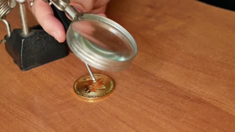 close-up-footage-of-man-making-fake-golden-bitcoin-coin-on-a-desk-with-magnifying-glass.-4k-video-of-counterfeiter