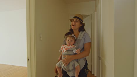 Happy-woman-with-baby-in-carrier-walking-around-an-empty-apartment