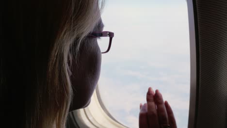 Eine-Frau-in-Gläsern-befasst-sich-mit-dem-Flugzeugfenster.-Silhouette,-Rückansicht