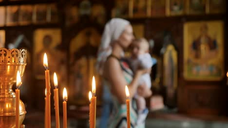 Brennende-Kerzen-in-der-Kirche,-Mutter-mit-Baby-auf-unscharfen-Hintergrund