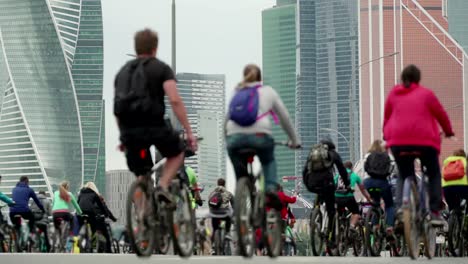 Bike-city-events-competition-in-background-of-skyscrapers,-crowd-of-cyclists-from-thousands-of-people-riding-bicycles,-unrecognizable-people-in-blur