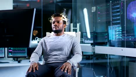 Hombre-usando-ondas-cerebrales-exploración-auricular-se-sienta-en-una-silla-mientras-viendo-estimulantes-imágenes-en-pantalla.-En-el-cerebro-moderno-estudio-laboratorio-monitores-Mostrar-EEG-lectura-y-modelo-de-cerebro.