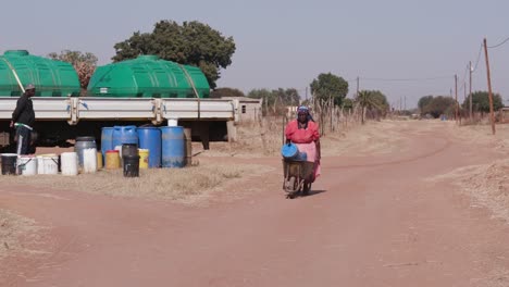 Una-mujer-africana-que-recoge-agua-de-una-cisterna-y-empujándolo-en-una-carretilla-a-su-casa