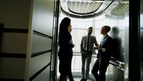 Tracking-shot-of-businesswomen-and-businessmen-colleagues-talking-in-elevator-and-prepare-to-move-down-in-modern-business-center