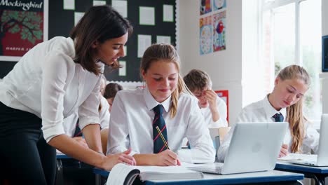 Teacher-Helping-Female-Pupil-Using-Computer-In-Classroom