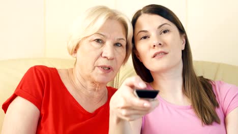 Mother-and-daughter-relaxing-on-sofa-at-home-watching-TV.-Switching-channels-with-remote-control