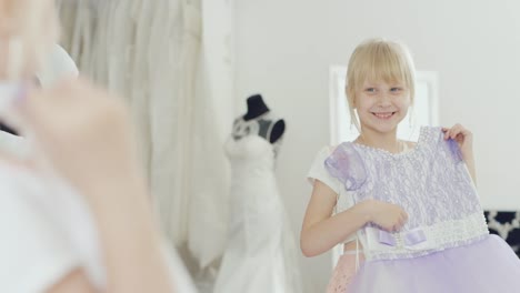 Rubia-niña-de-6-años-mira-su-nuevo-vestido-elegante.-Ve-un-reflejo-en-el-espejo