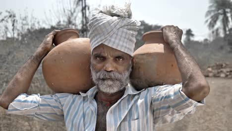 Tired-poor-man-carrying-clay-pots-and-standing-in-barren-farmland-under-the-hard-sun