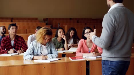 SchülerInnen-und-Schüler-haben-Unterricht-mit-Lehrer,-junge-Menschen-schreiben-und-reden-zu-sitzen-an-Tischen-tutor.-Millennials,-Bildung-und-Hochschulen-Konzept.