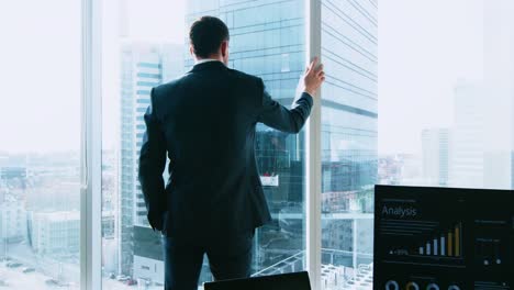 Zuversichtlich-Geschäftsmann-in-einem-Anzug-zu-Fuß-durch-sein-Büro-und-Suche-aus-dem-Fenster-nachdenklich.-Stilvolle-moderne-Business-Office-mit-PC-und-Blick-auf-die-große-Stadt.