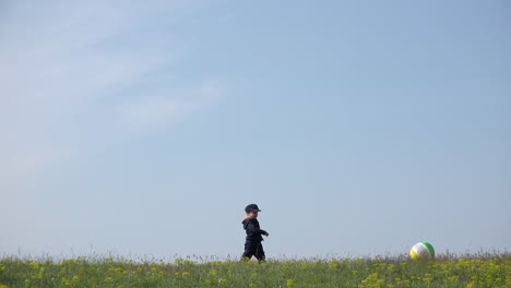 Kleine-Jungen-spielen-mit-großen-Ball-auf-Bergrücken,-heiteren-Himmel-über-4K