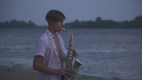 Handsome-young-guy-is-playing-the-saxophone-on-the-river-bank