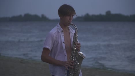 Handsome-young-guy-is-playing-the-saxophone-on-the-river-bank