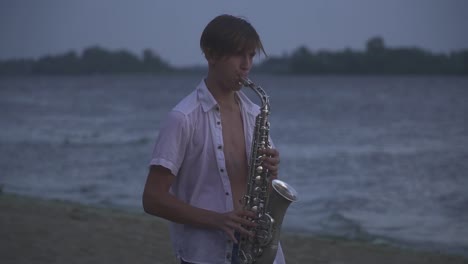 Chico-joven-guapo-es-jugar-el-saxophone-en-la-orilla-del-río