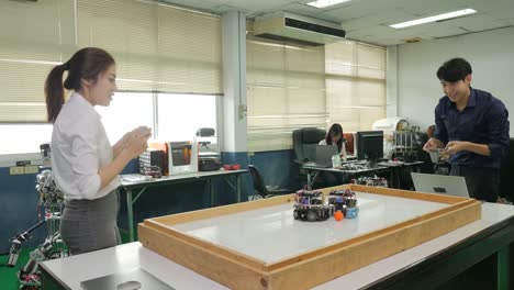 Two-electronics-engineer-programming-and-control-robots-to-playing-soccer-with-mobile-phone-in-the-workshop.-People-with-technology-or-innovation-concept.