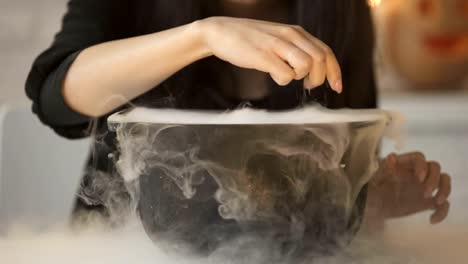 Witch-conjuring,-putting-magic-spell-and-cooking-potion-in-pot-with-white-smoke