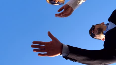 Successful-business-partners-standing-and-stacked-hands-together-on-blue-sky-background.-Young-colleagues-putting-their-arms-in-centre-as-symbol-of-unity-and-teamwork.-Slow-motion-Low-angle-view