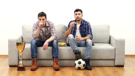 Die-beiden-Männer-schauen-Fußball-auf-dem-Sofa-und-Essen-chips