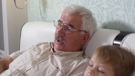 Senior-hombre-acostado-en-cama-y-viendo-la-televisión-con-su-nieto