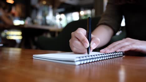 Slow-Motion-von-Frauenhand-schreiben-auf-leere-Notebooks-auf-Holztisch-im-café