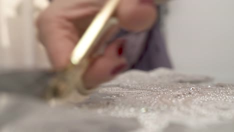 A-closeup-of-woman's-hands-cutting-out-sequined-and-beaded-lace-following-its-shape-and-putting-the-scissors-on-the-table-in-the-end