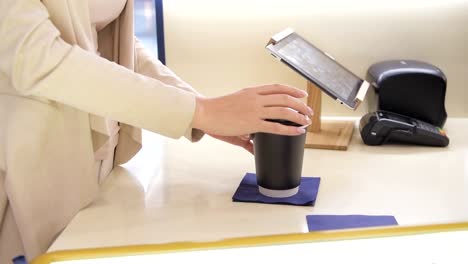 Slow-motion-close-up-shot-of-a-young-woman-buys-coffee-and-closes-cap-on-black-paper-cup-at-coffee-bar