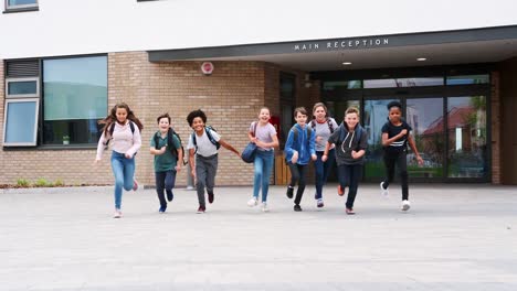 Grupo-de-estudiantes-de-secundaria-en-funcionamiento-fuera-de-los-edificios-escolares-a-la-cámara-al-final-de-clase