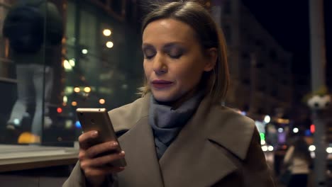 Elegant-young-lady-reading-message-on-smartphone-while-walking-on-city-street