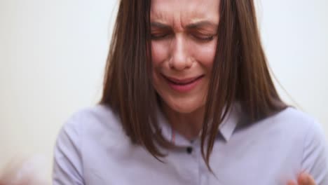 A-closeup-of-brunette's-face-with-closed-eyes,-she-seems-to-by-crying-and-shrugging.-She-sneezes-and-wipes-off-her-nose.