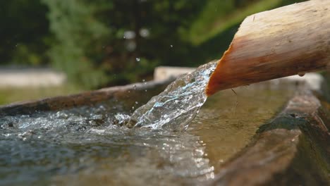 SLOW-MOTION:-Crystal-clear-stream-water-flows-through-the-wooden-pipe-into-basin