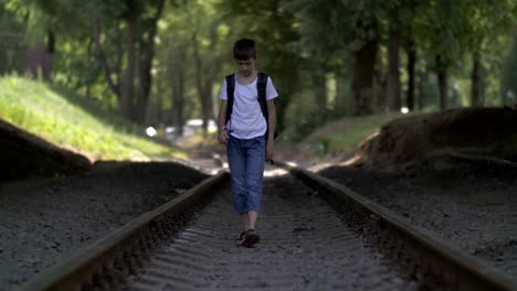 offended-boy-in-depression-walks-along-the-railway-track,-bowing-head,-regrets-for-action,-deep-reflection,-not-successful-first-love-concept,-outdoors