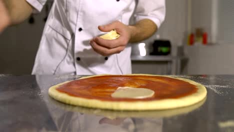 Hand-Chef-legt-Käse-in-Pizza-basieren-auf-Tomaten-Soße-Nahaufnahme