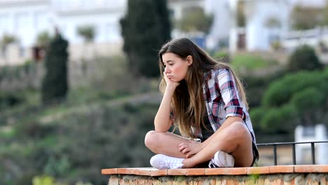 Bored-teen-complaining-sitting-on-a-ledge-in-a-town