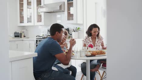 Familia-joven-sentada-a-la-mesa-en-la-cocina-comiendo-juntas,-enfoque-selectivo,-tiro-panorámico