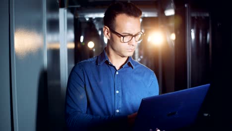 One-programmer-walks-in-a-server-room-with-a-laptop-in-hands,-close-up.