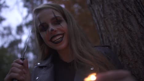 Young-pretty-blonde-girl-with-horrifying-Halloween-make-up-holding-hatchet-and-small-candle-in-hands.