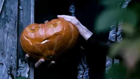 A-young-woman-with-halloween-make-up-holding-a-pumpkin-with-a-burning-candle.-4K