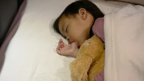 Asian-mother-is-putting-blanket-on-her-daughter-who-is-sleeping-in-the-bed-and-goodnight-kiss-with-love.-Health-care-concept.