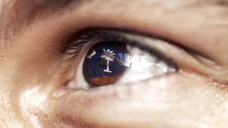 Man-with-brown-eye-in-close-up,-the-flag-of-South-Carolina-state-in-iris,-united-states-of-america-with-wind-motion.-video-concept