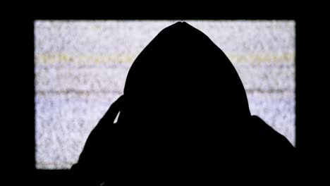 Silhouette-of-Man's-Head-in-Hood-is-Watching-White-Static-Noise-and-TV-Interference