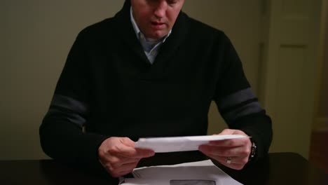 A-man-looking-over-bills-at-the-table,-looking-stressed-and-throwing-paper